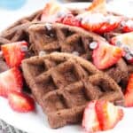 A plate of Chocolate Waffles topped with sliced strawberries and chocolate chips creates a deliciously rich breakfast treat.