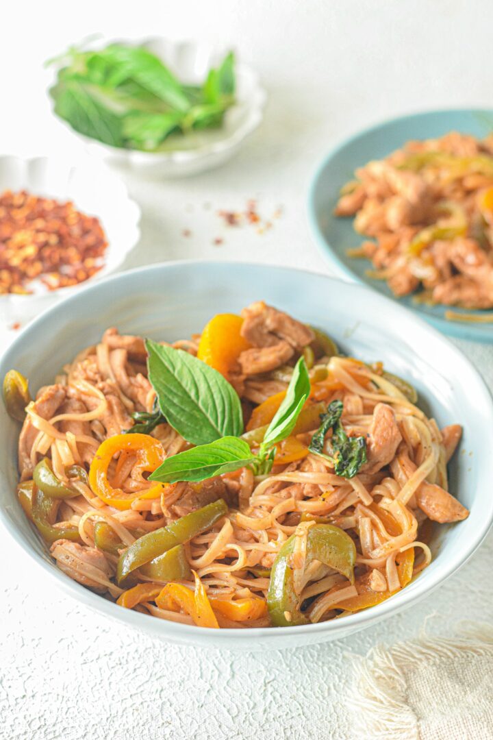 drunken chicken noodles in a white bowl with fresh herbs on top.
