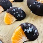 Chocolate Covered Oranges: Orange segments partially dipped in dark chocolate and sprinkled with sea salt, arranged on a wooden surface.