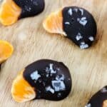 Chocolate Covered Oranges: Tangerine slices partially dipped in dark chocolate and sprinkled with coarse sea salt, arranged on a wooden surface.