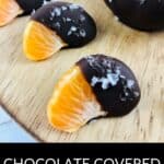 Chocolate Covered Oranges: Tangerine segments partially dipped in dark chocolate and topped with sea salt, arranged artfully on a wooden surface.