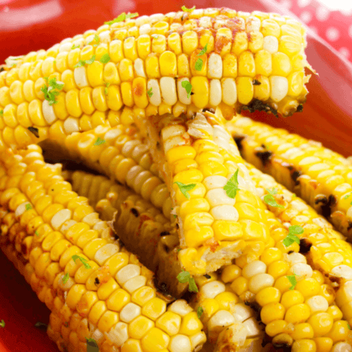 Grilled corn ribs with charred kernels and a touch of garlic butter, sprinkled with green herbs and served on a red plate.