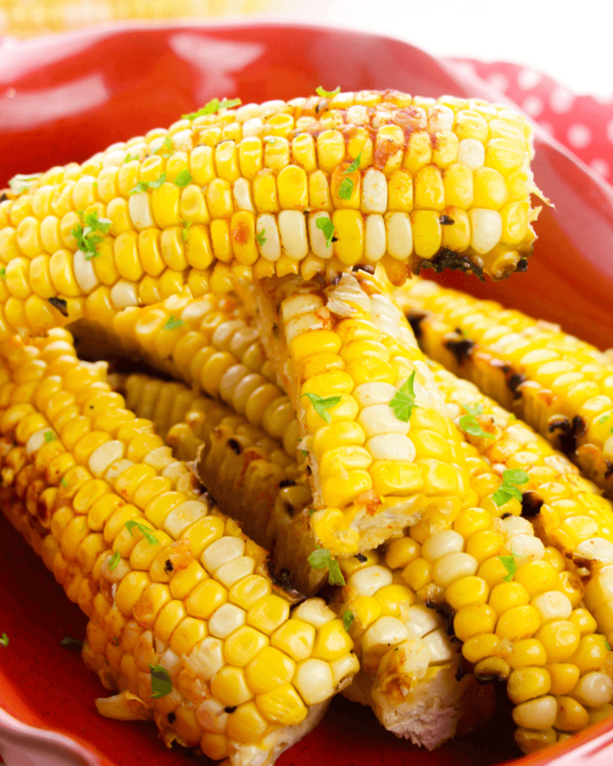 Grilled corn ribs with charred kernels and a touch of garlic butter, sprinkled with green herbs and served on a red plate.