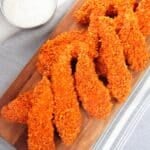 A wooden board with tenders, served with a bowl of white dipping sauce on the side.