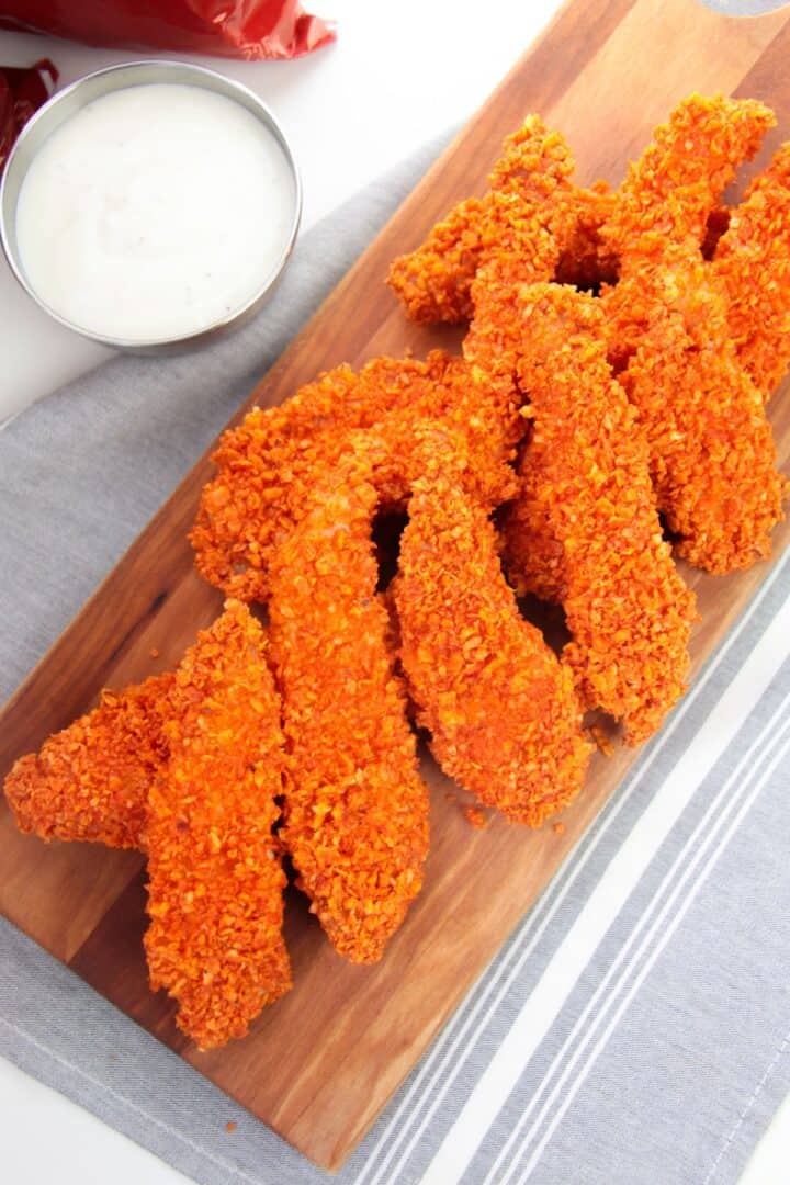 A wooden board with tenders, served with a bowl of white dipping sauce on the side.
