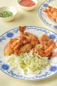 A plate of crispy Panko Shrimp served with shredded cabbage, with dipping sauces in small bowls in the background.