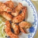 A plate of crispy panko shrimp with sliced cabbage on a blue and white floral dish, served alongside a small bowl of chopped green onions.