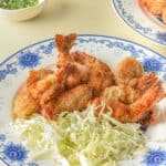 A plate with the seafood and shredded cabbage, served with bowls of dipping sauce and chopped green onions in the background.