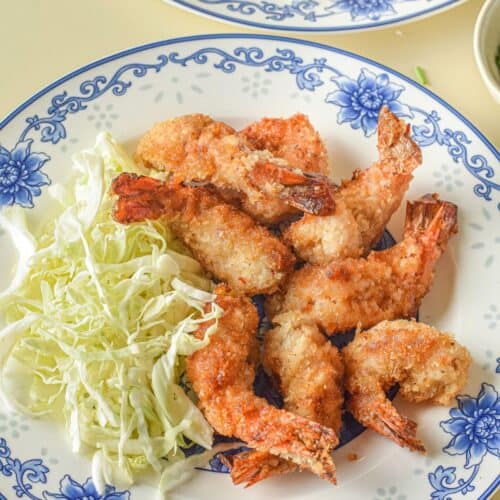 A plate with crispy panko shrimp and a serving of shredded cabbage, beautifully arranged on a floral-patterned dish.