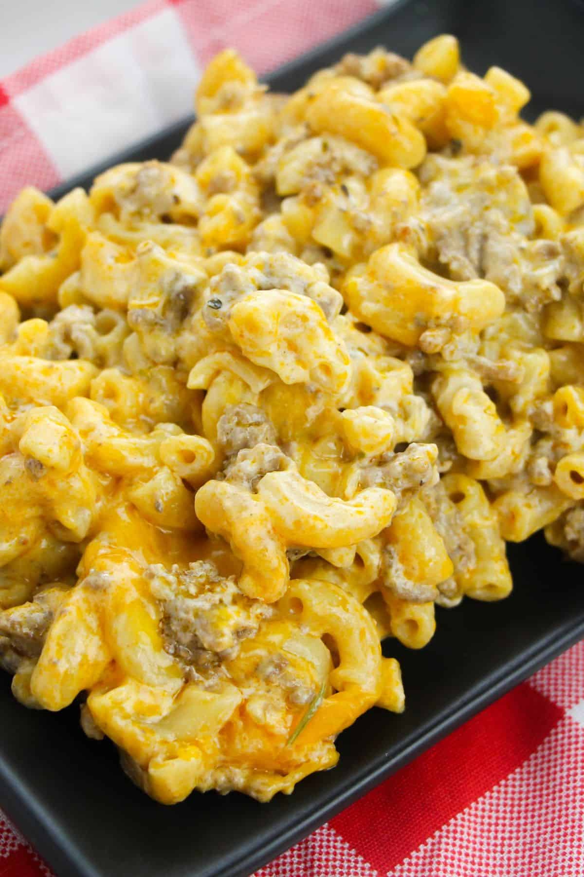 A close-up of homemade dish mixed with ground beef, served on a black plate with a red and white checkered cloth underneath.