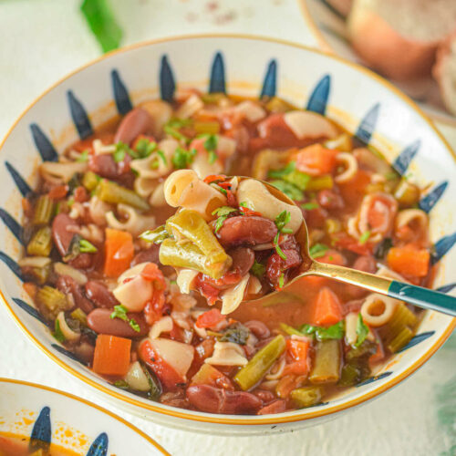 Italian Minestrone Soup in a white dish with a spoon in it.