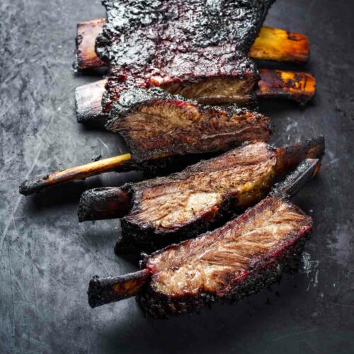 Several bbq beef ribs sit on a black cutting board