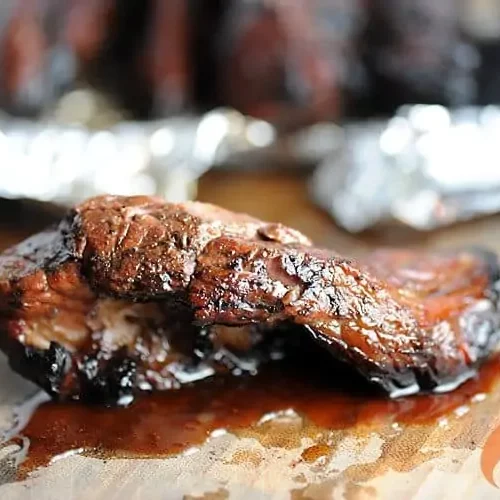 A closeup of a grilled beef rib sits in front of some foil