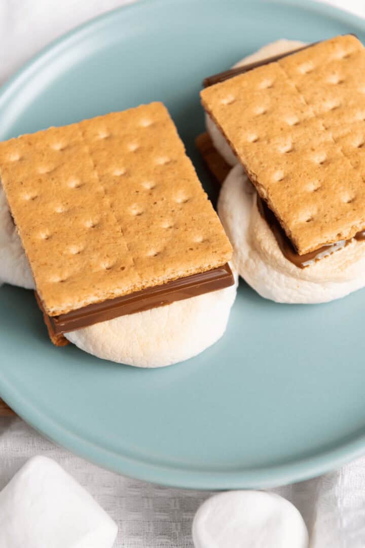 A blue plate displays two air fryer s'mores made with graham crackers, melted chocolate, and toasted marshmallows.
