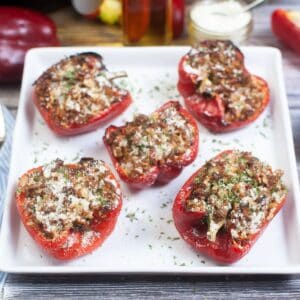 Five Air Fryer Stuffed Peppers, halved and filled with a browned, crumbly mixture and topped with grated cheese, are arranged on a white square plate.