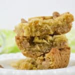 Three stacked snacks with visible white chocolate chips rest on a white plate, with a green cloth blurred in the background.
