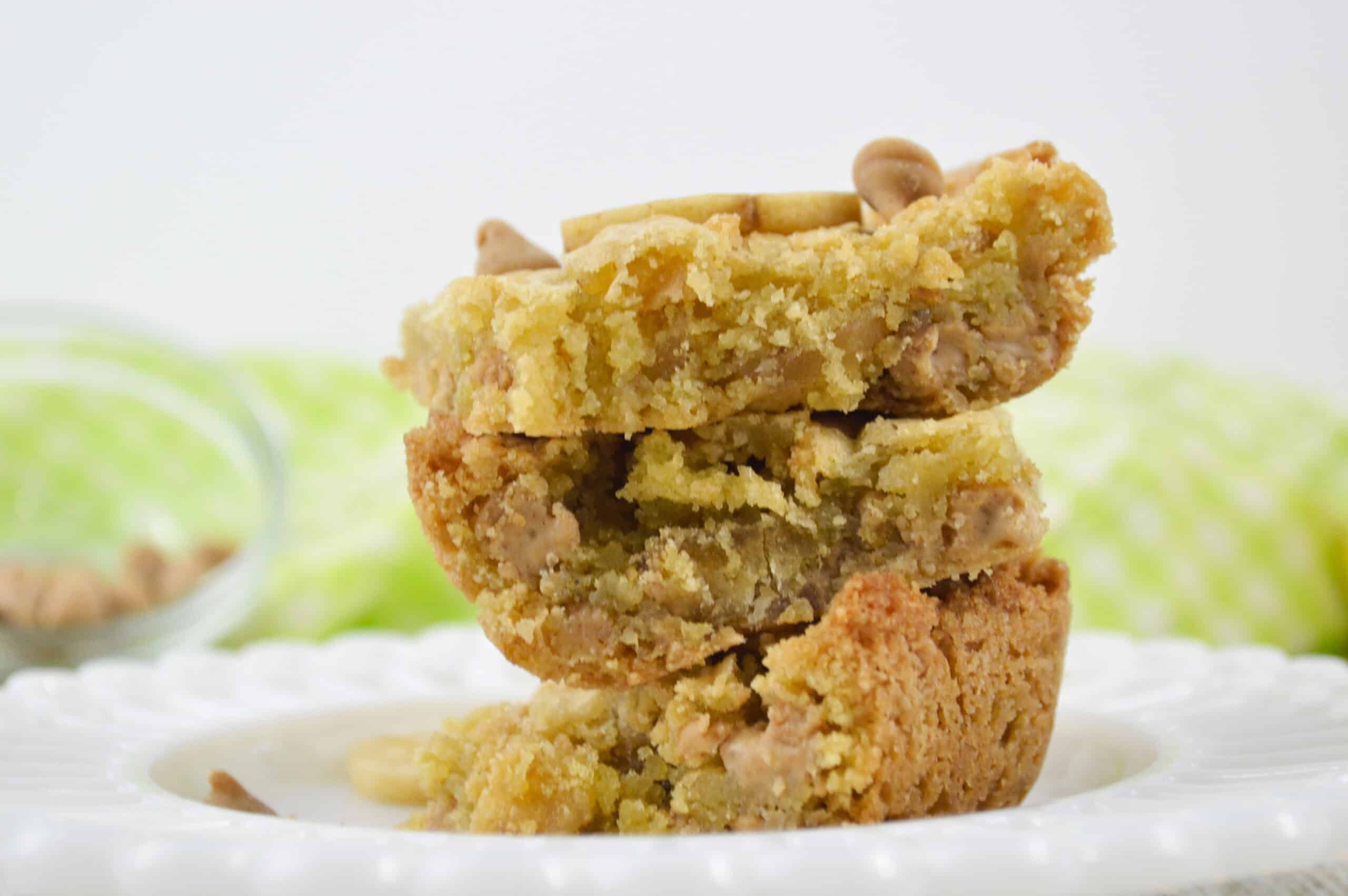 Three stacked snacks with visible white chocolate chips rest on a white plate, with a green cloth blurred in the background.