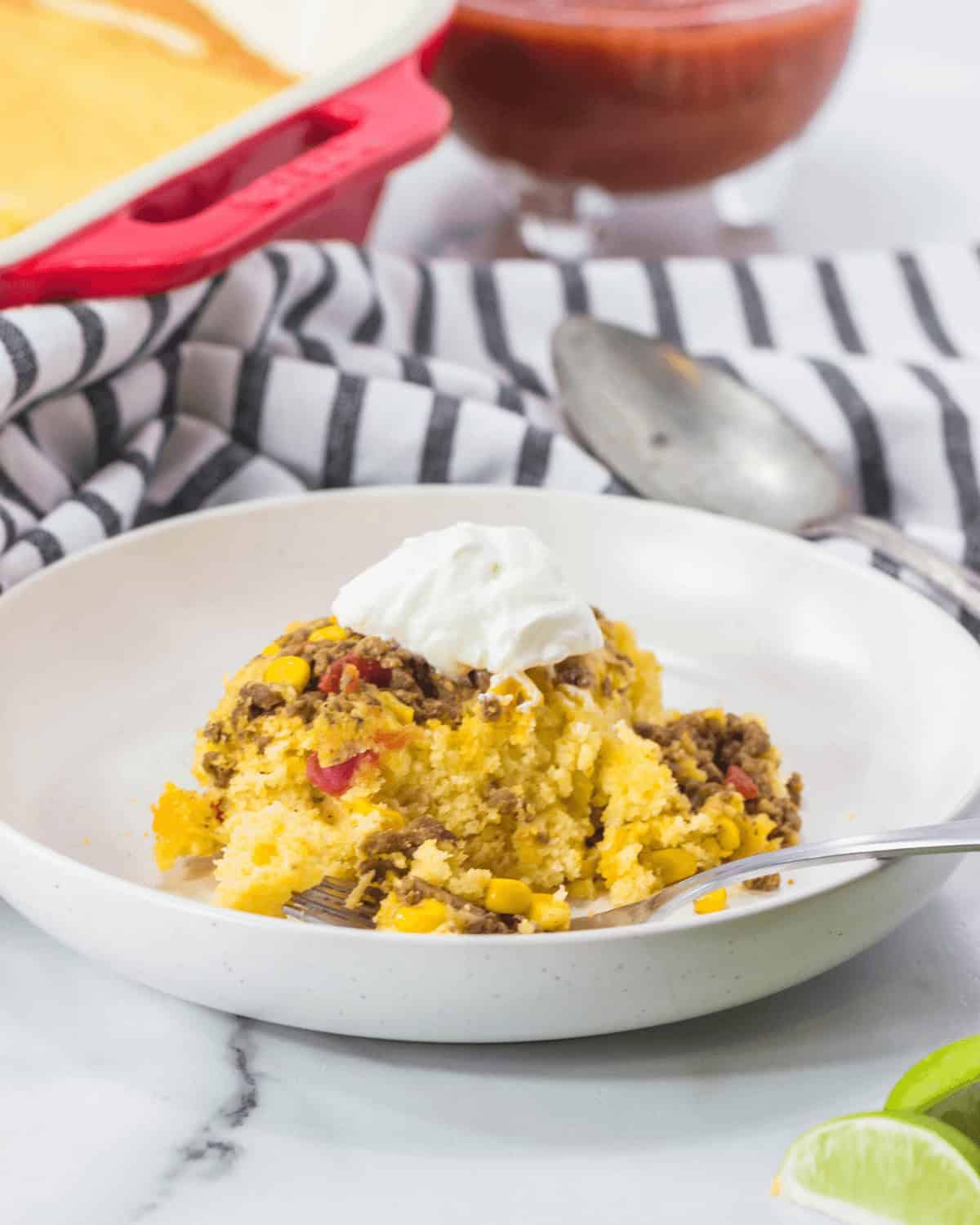 A bowl of the meal topped with sour cream, accompanied by salsa and a napkin on a marble table.
