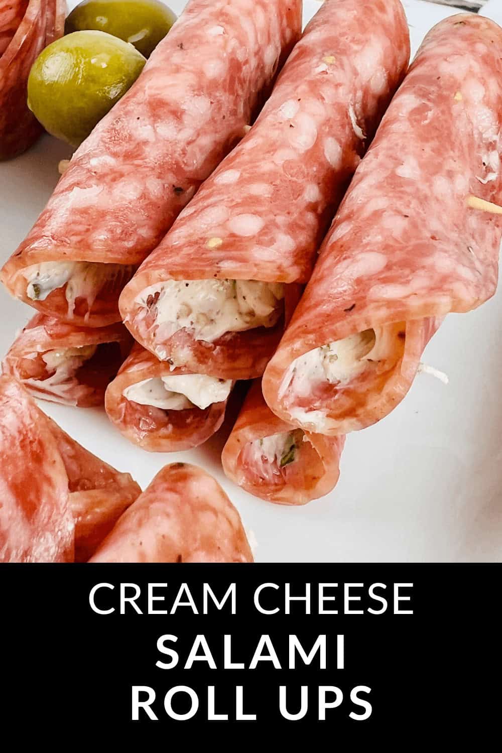 A plate of Salami Roll Ups brimming with creamy cheese, accompanied by a side of green olives.