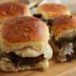 Four Beef Sliders with melted cheese on soft buns are arranged on a wooden board, perfect for sharing.