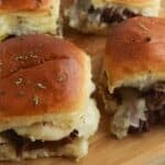 Four sandwiches on a wooden cutting board, topped with fresh herbs and served on soft, golden buns.