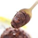 A spoon holding a portion of rich, edible brownie batter, with more dough blurred in the background.