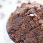 A close-up of edible brownie batter with chocolate chips mixed in, resting in a white bowl.