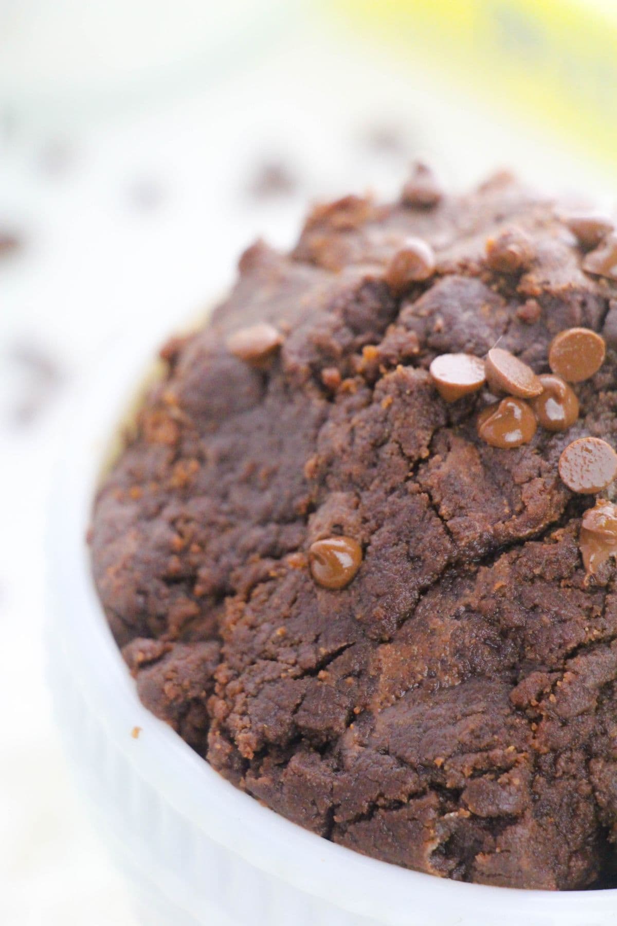 A close-up of edible brownie batter with chocolate chips mixed in, resting in a white bowl.