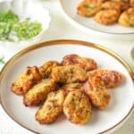 A white plate holds several golden-brown homemade tater tots; more fritters, chopped herbs, and dipping sauce are visible in the background.