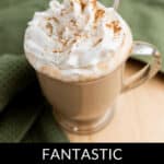 A glass mug filled with iced pumpkin spice latte topped with whipped cream and cinnamon sits on a wooden surface next to a green fabric. Text below reads, "Fantastic Iced Pumpkin Spice Latte.