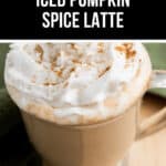 A glass cup filled with an Iced Pumpkin Spice Latte, topped with whipped cream and sprinkled with cinnamon.