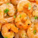 Roasted shrimp garnished with chopped parsley, served on a bed of white rice on a black plate.