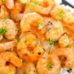 Roasted shrimp garnished with chopped parsley served on a bed of white rice on a black rectangular plate.