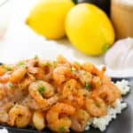 A plate served over rice, garnished with herbs. Lemons, garlic, and other ingredients are visible in the background.