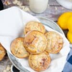 A plate of five glazed Lemon Poppy Seed Cupcakes sits on a white napkin, with a bottle of milk and whole lemons nearby on a rustic wooden table.
