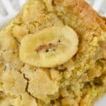 A close-up of a crumbly Peanut Butter Banana Bar topped with a dried banana slice on a white surface.
