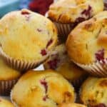 A close-up of Raspberry White Chocolate Muffins, showcasing a pile of golden-brown treats with visible pieces of raspberries and white chocolate in paper liners.