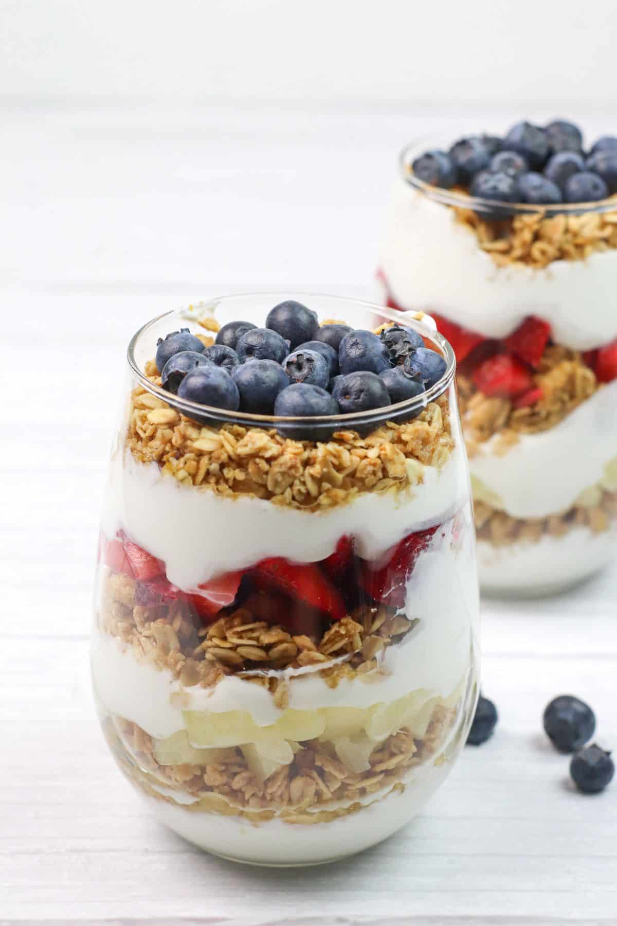 A glass filled with layers of granola, strawberries, and blueberries creates a delicious dessert.