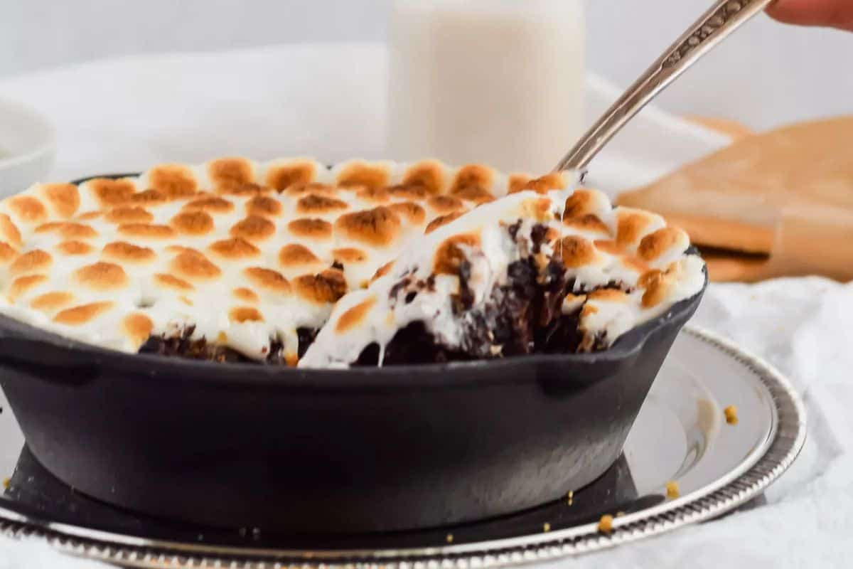 A brownie skillet topped with toasted marshmallows, chunks of chocolate, and pieces of graham cracker.