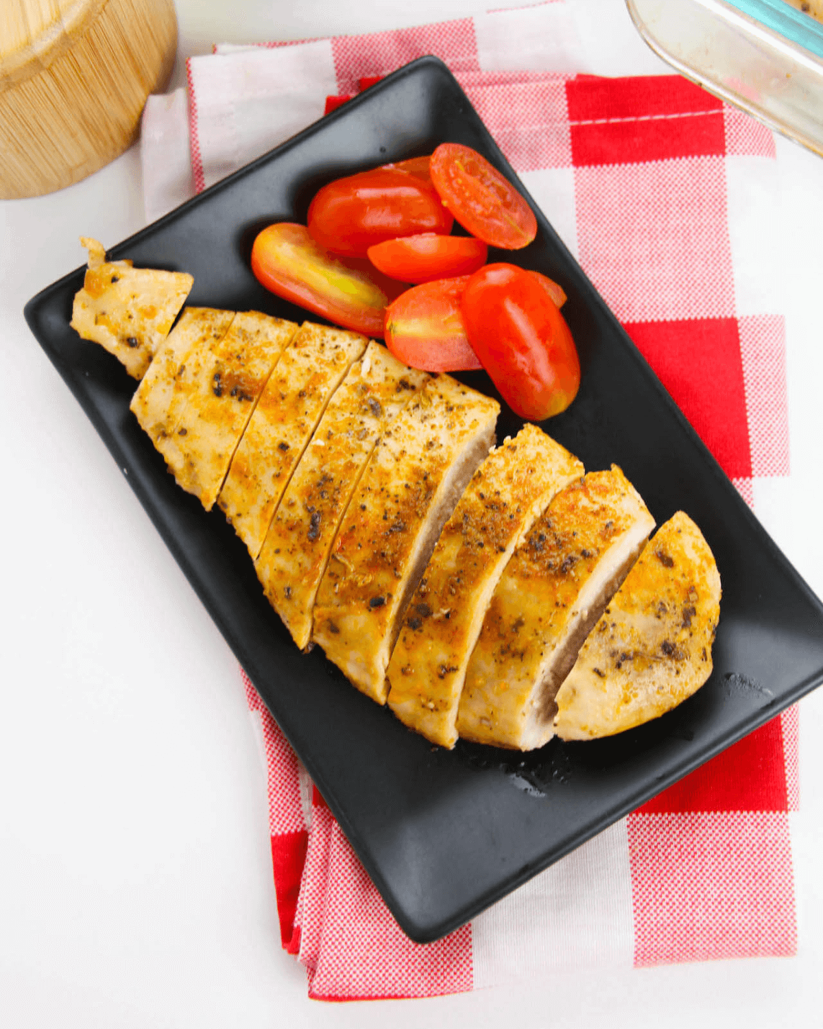 Baked chicken cutlets on a black plate with tomatoes.