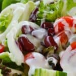 A close-up of a fresh salad with lettuce, kidney beans, sliced cucumber, cherry tomatoes, and a drizzle of Panera Green Goddess Dressing.
