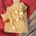 A slice topped with whole peanuts rests on a wooden board, set atop a red striped cloth on a rustic wooden surface.