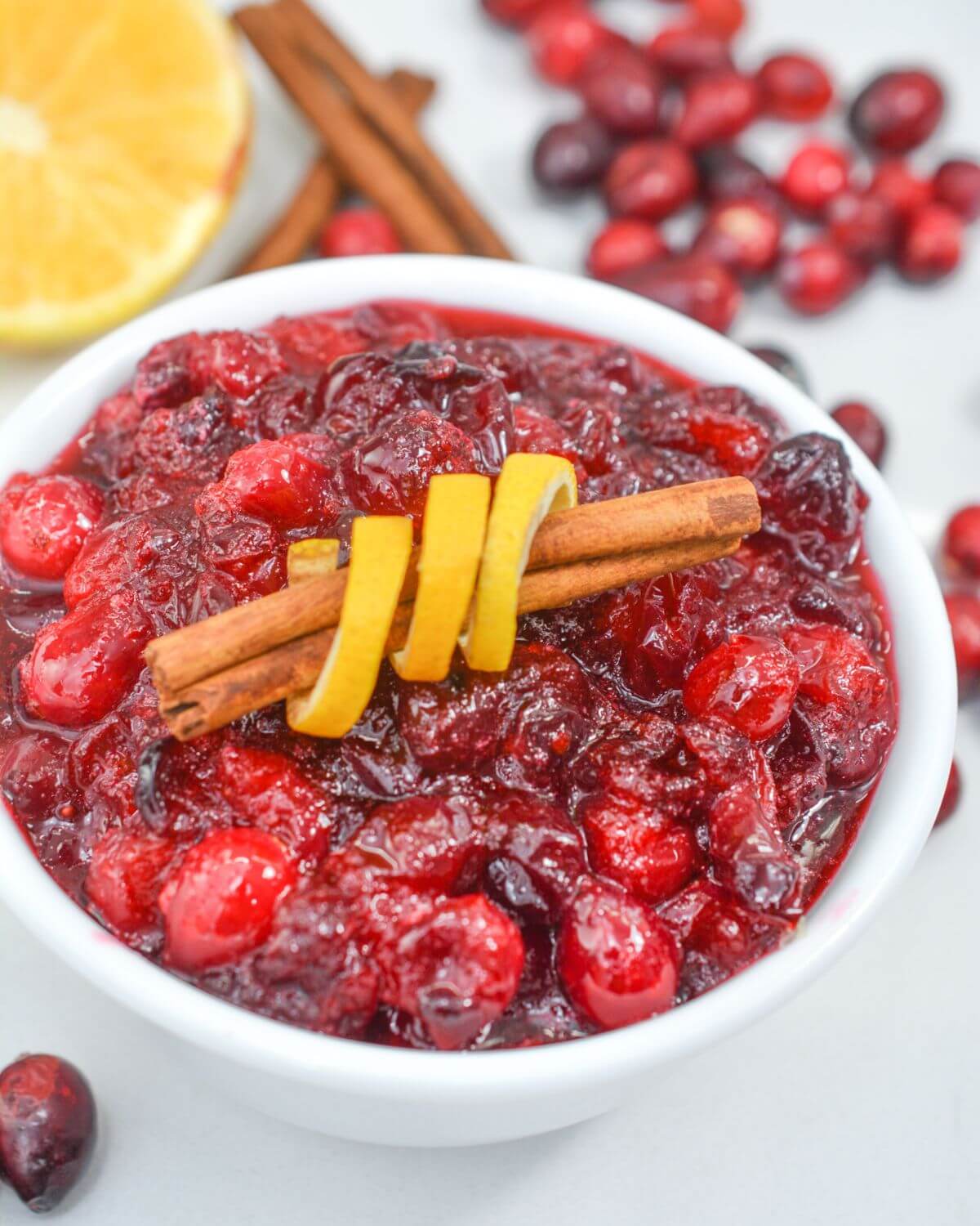 Homemade Ocean Spray Cranberry Sauce in a white bowl with a cinnamon stick wrapped in orange peel.