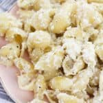 A plate cheese sauce, sprinkled with black pepper, sits on a pink dish next to a striped cloth.