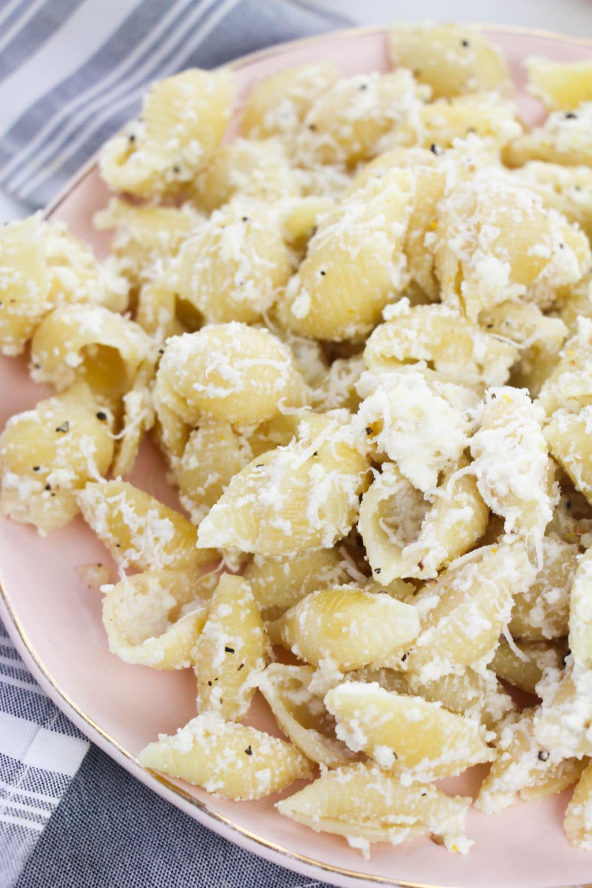 A plate cheese sauce, sprinkled with black pepper, sits on a pink dish next to a striped cloth.