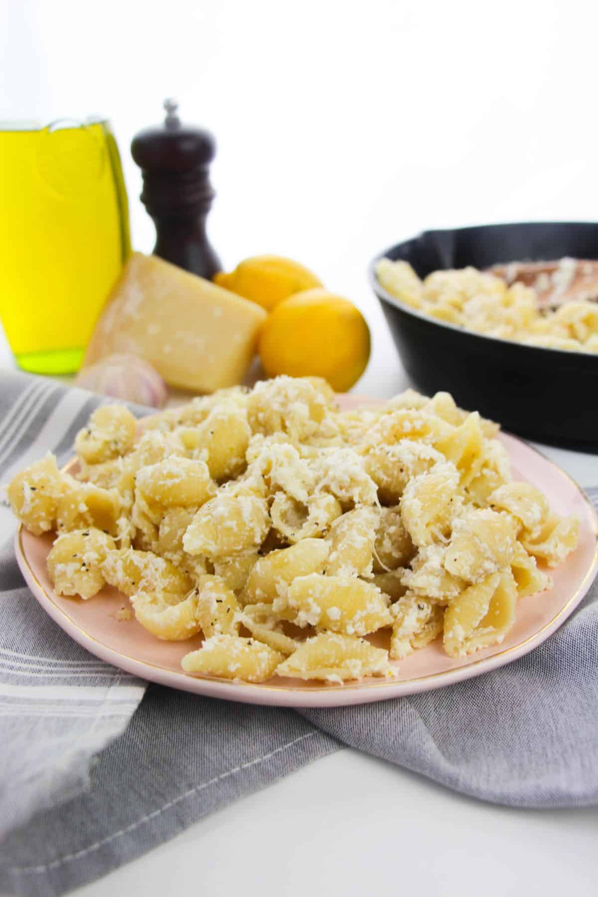 A plate of shells with a creamy cheese sauce sits on a gray cloth.