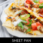 A sheet pan holds a vibrant plate of loaded nachos, generously topped with melted cheese, juicy tomatoes, crisp onions, and fresh cilantro.