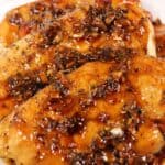 Cooked chicken breasts topped with a glossy garlic herb sauce are arranged on a white plate, reminiscent of classic Baked Honey Garlic Chicken.