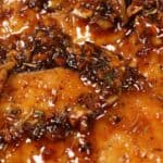 Close-up of Baked Honey Garlic Chicken breast topped with a glossy, herb and spice sauce containing visible pieces of garlic and herbs.
