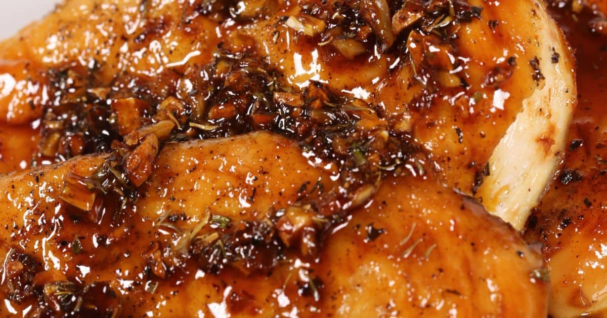 Close-up of Baked Honey Garlic Chicken breast topped with a glossy, herb and spice sauce containing visible pieces of garlic and herbs.